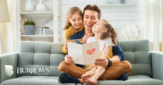 Father reading a loving card and holding his two daughters
