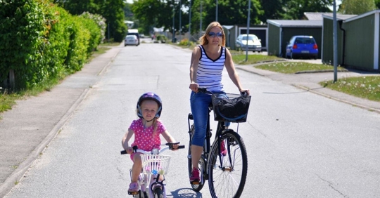 A girl and her mother riding bicycles down a residential street