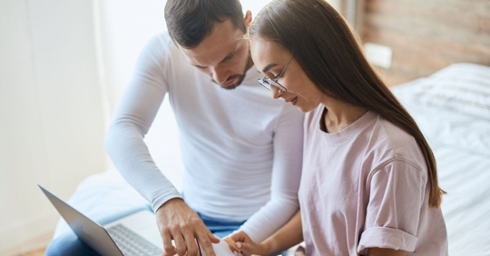 A man and a woman sitting together looking at a laptop, as if they're reviewing something important.